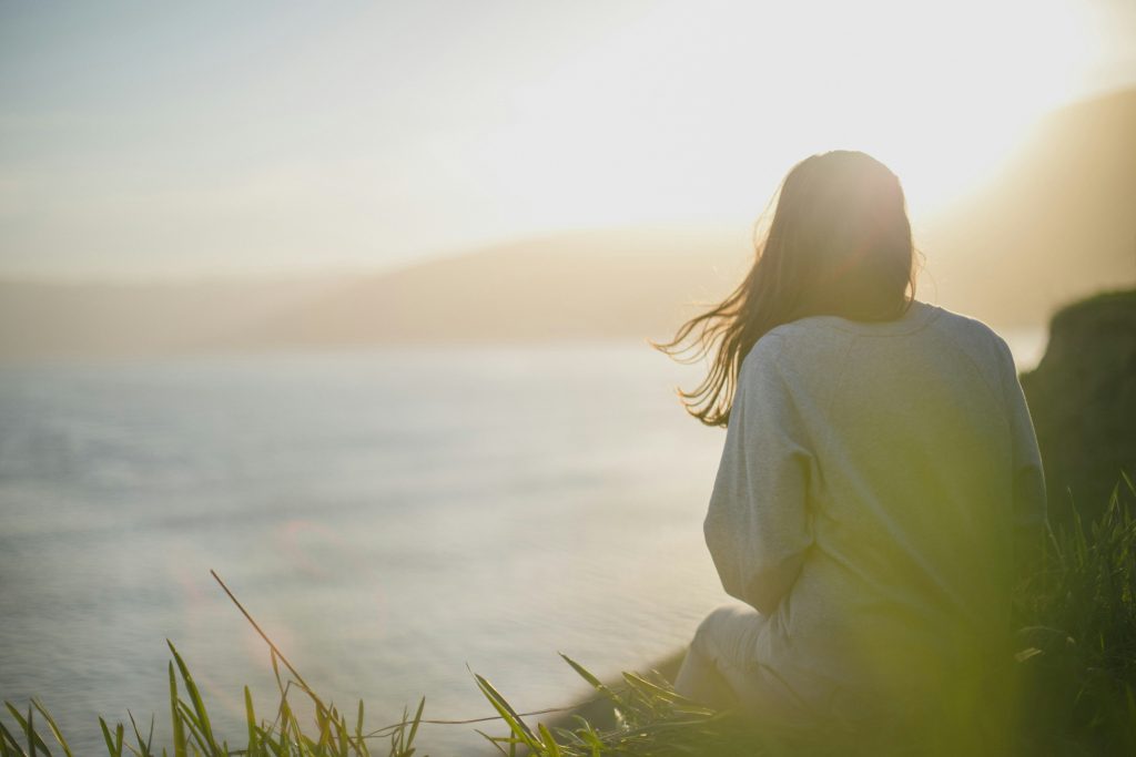 Woman sitting quietly by the sea at sunrise, a moment of calm amid uncertainty